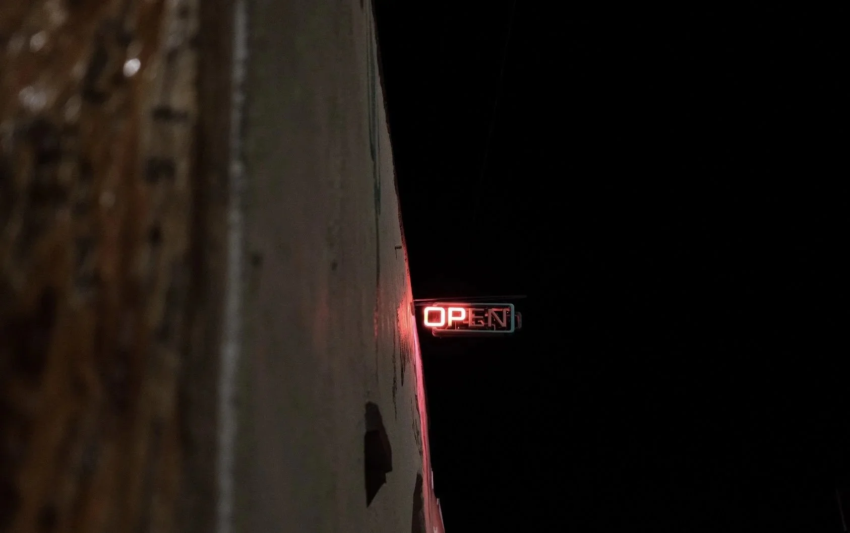 A neon OPEN sign glowing on a dark alley wall at night